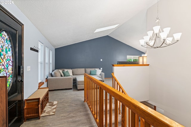 hall with an upstairs landing, a textured ceiling, wood finished floors, a chandelier, and vaulted ceiling