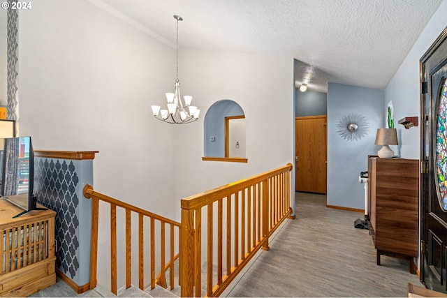 hallway with wood finished floors, baseboards, an inviting chandelier, a textured ceiling, and an upstairs landing