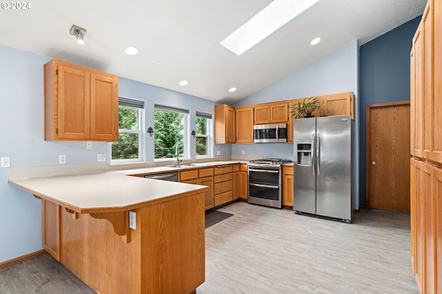 kitchen with lofted ceiling with skylight, light countertops, appliances with stainless steel finishes, a peninsula, and light wood-style floors