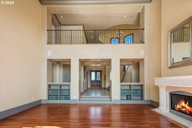 unfurnished living room with a towering ceiling, a chandelier, and wood-type flooring