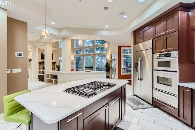 kitchen with appliances with stainless steel finishes, a center island, light stone counters, and hanging light fixtures