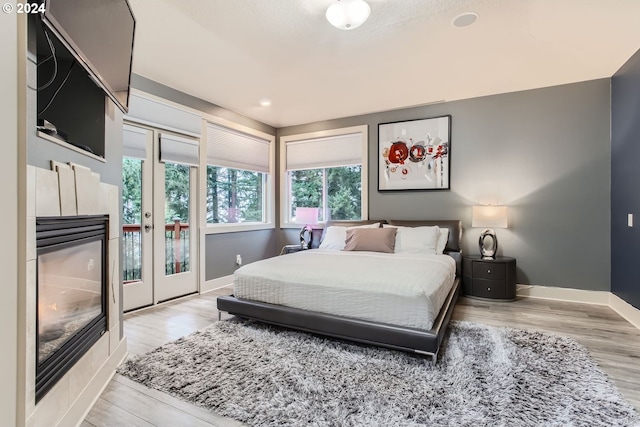 bedroom featuring light hardwood / wood-style floors, access to exterior, and a tiled fireplace