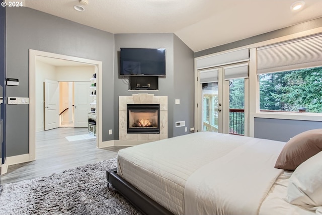 bedroom featuring access to exterior, a fireplace, vaulted ceiling, and light wood-type flooring