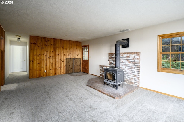 unfurnished living room with carpet flooring, a wood stove, a textured ceiling, and wooden walls