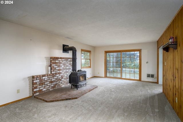 unfurnished living room featuring wood walls, a wood stove, a textured ceiling, and light carpet