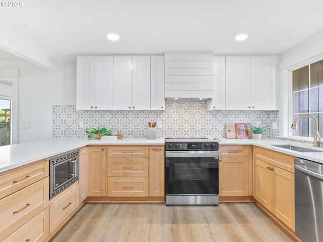 kitchen featuring appliances with stainless steel finishes, light brown cabinetry, tasteful backsplash, sink, and light hardwood / wood-style flooring