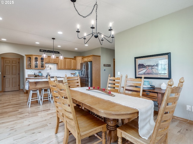 dining room with light wood-type flooring, recessed lighting, arched walkways, and a notable chandelier