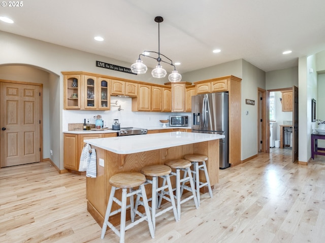 kitchen featuring arched walkways, light countertops, light wood-style floors, stainless steel appliances, and a kitchen island