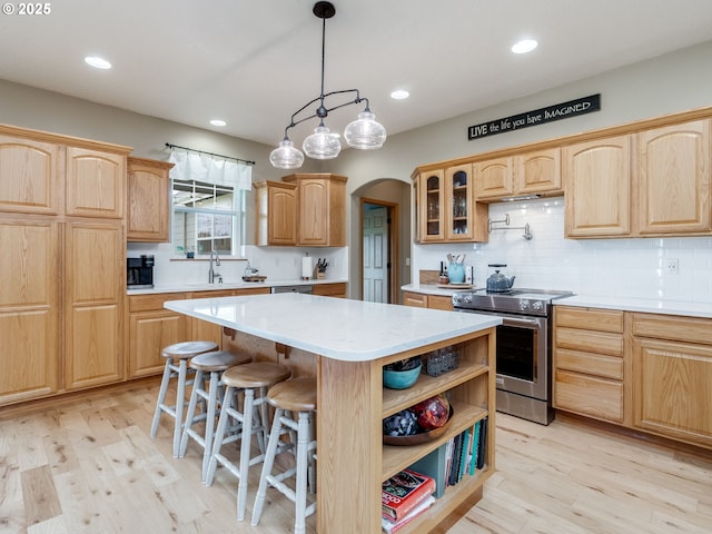 kitchen featuring light brown cabinets, a center island, light countertops, stainless steel electric stove, and arched walkways