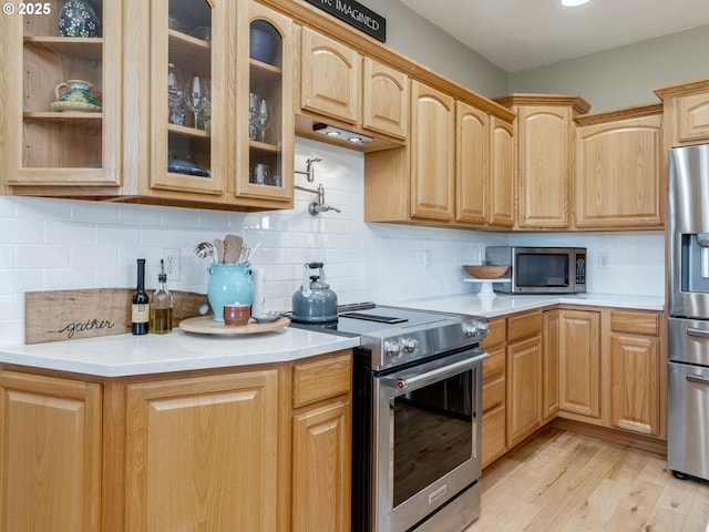 kitchen with glass insert cabinets, light brown cabinetry, light countertops, stainless steel appliances, and light wood finished floors