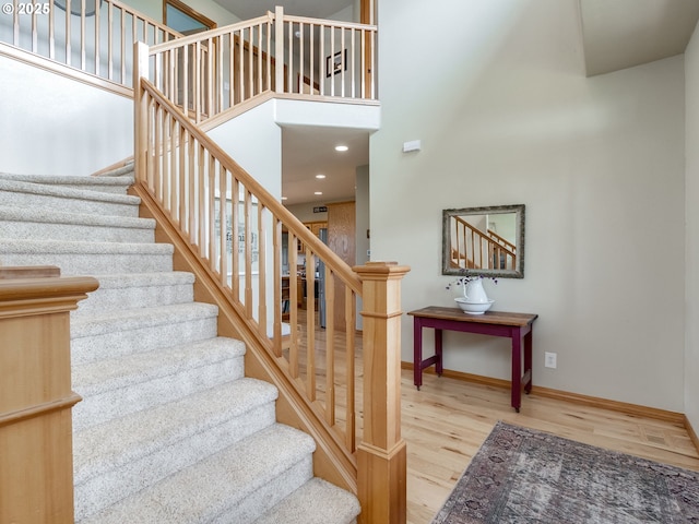 stairway featuring a high ceiling, baseboards, and wood finished floors