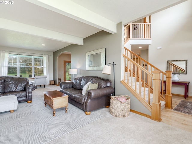 carpeted living room featuring baseboards, arched walkways, beamed ceiling, stairway, and recessed lighting