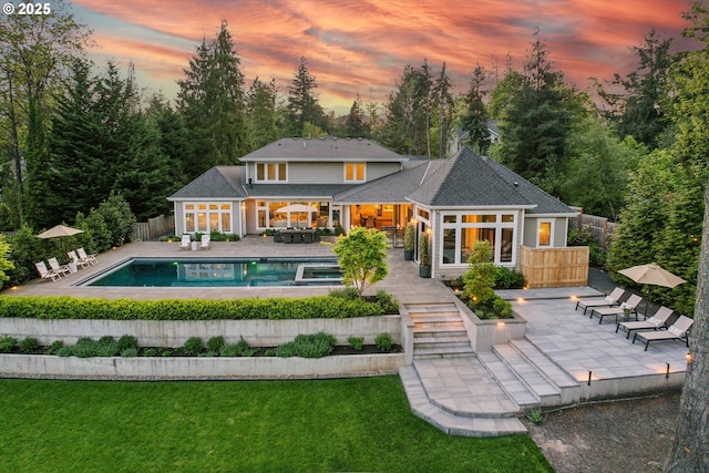 back of house at dusk featuring a lawn, a fenced in pool, a fenced backyard, and a patio area