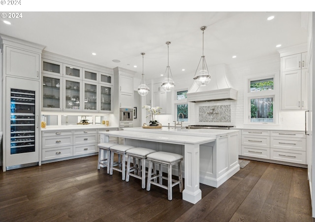 kitchen with custom range hood, white cabinets, wine cooler, a breakfast bar area, and an island with sink