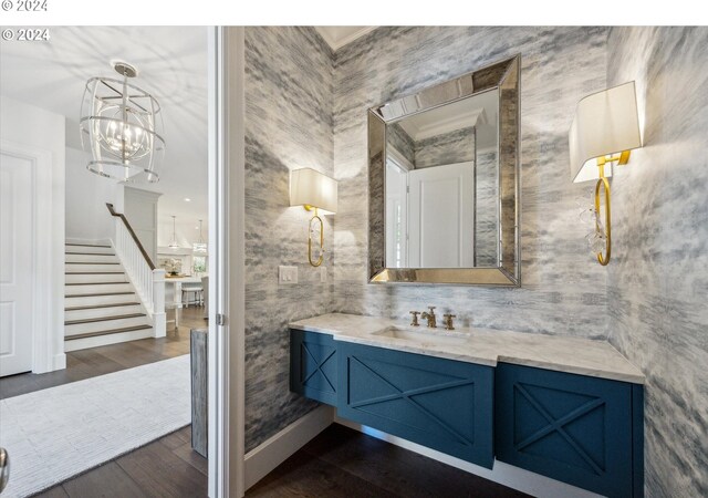 bathroom featuring baseboards, wallpapered walls, wood finished floors, and vanity