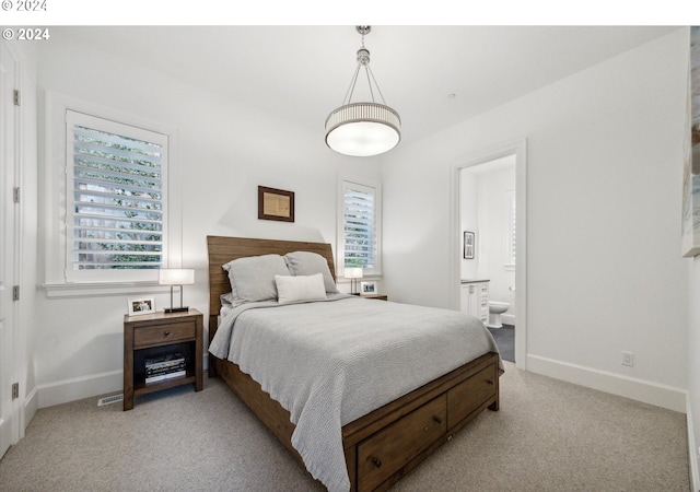 bedroom with baseboards, connected bathroom, and light colored carpet