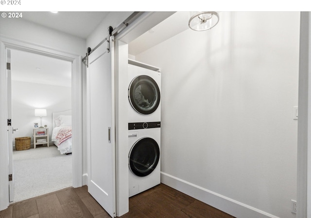 laundry room with stacked washer / drying machine, a barn door, and dark wood-type flooring