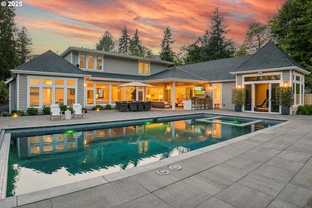 pool at dusk featuring an outdoor hangout area, an outdoor kitchen, a pool with connected hot tub, and a patio area