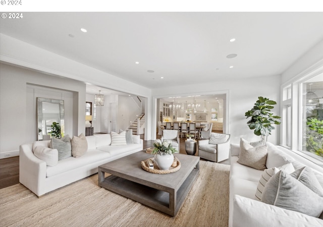 living room with light wood-type flooring, recessed lighting, an inviting chandelier, and stairway