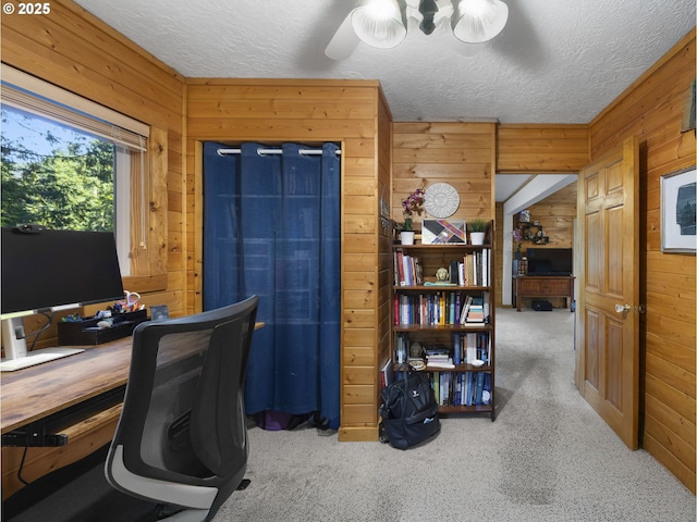 home office with a textured ceiling, wooden walls, and carpet flooring