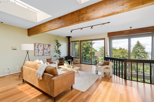 living room with a wood stove, rail lighting, a skylight, beamed ceiling, and light hardwood / wood-style flooring