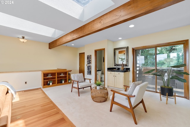 interior space with a skylight, beam ceiling, and light hardwood / wood-style flooring