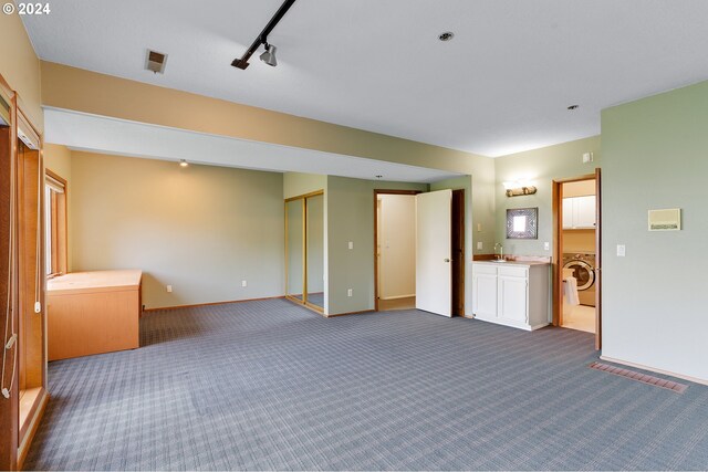 unfurnished bedroom featuring washer / dryer, sink, rail lighting, and carpet floors