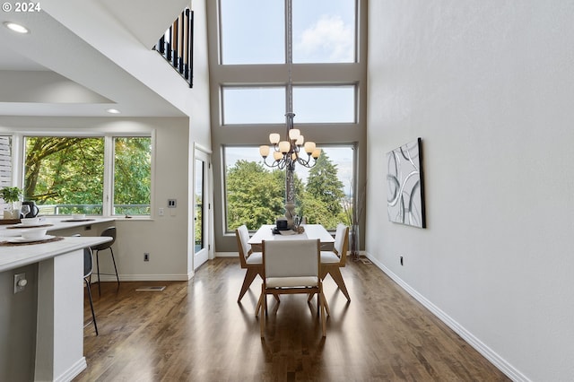 dining space with wood-type flooring, a towering ceiling, and a chandelier