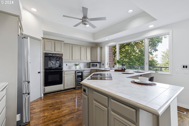 kitchen with a center island, dark hardwood / wood-style floors, black appliances, a raised ceiling, and tile countertops