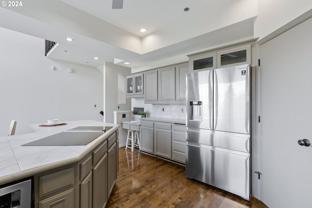 kitchen with gray cabinets, black electric cooktop, tasteful backsplash, dark hardwood / wood-style floors, and stainless steel fridge