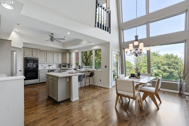 dining area featuring ceiling fan with notable chandelier, dark hardwood / wood-style flooring, sink, and a tray ceiling