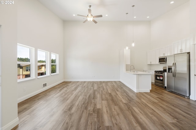 unfurnished living room featuring ceiling fan, light hardwood / wood-style flooring, a high ceiling, and sink