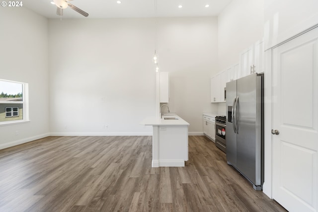 kitchen with hardwood / wood-style floors, a high ceiling, white cabinets, hanging light fixtures, and appliances with stainless steel finishes