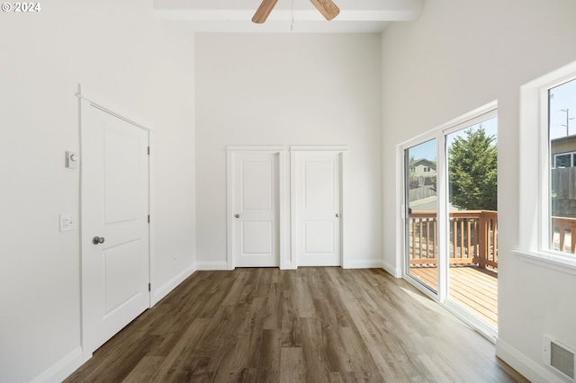 interior space with ceiling fan, a towering ceiling, beamed ceiling, and dark hardwood / wood-style floors