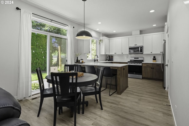 kitchen featuring white cabinets, sink, decorative light fixtures, light hardwood / wood-style floors, and stainless steel appliances