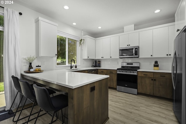 kitchen with white cabinets, dark brown cabinets, light wood-type flooring, and stainless steel appliances