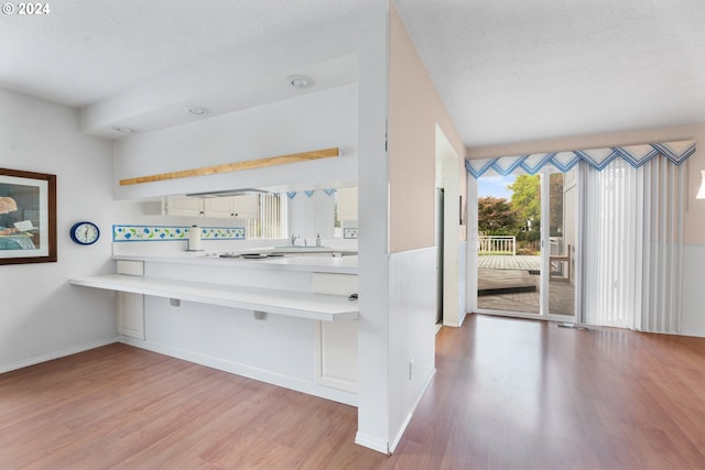 kitchen with kitchen peninsula, a textured ceiling, light hardwood / wood-style floors, and a breakfast bar area