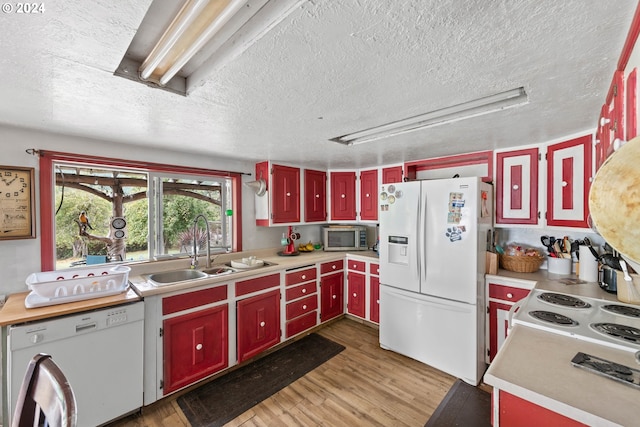 kitchen with white appliances, red cabinets, a sink, and light wood-type flooring