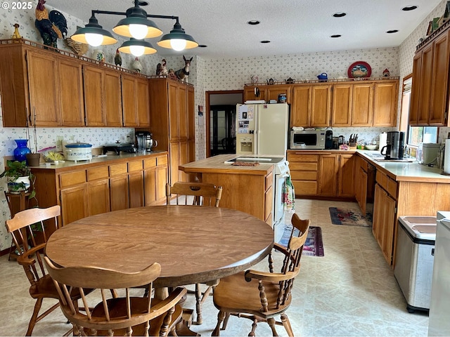 kitchen with brown cabinets, a kitchen island, white appliances, wallpapered walls, and light floors