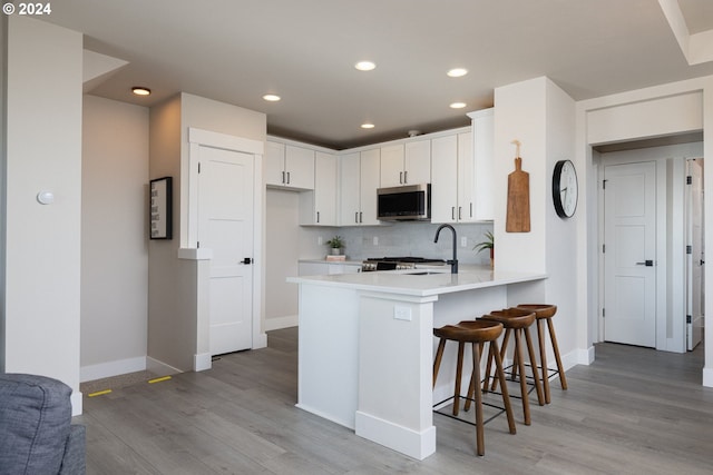 kitchen with white cabinets, kitchen peninsula, backsplash, a breakfast bar, and light hardwood / wood-style flooring