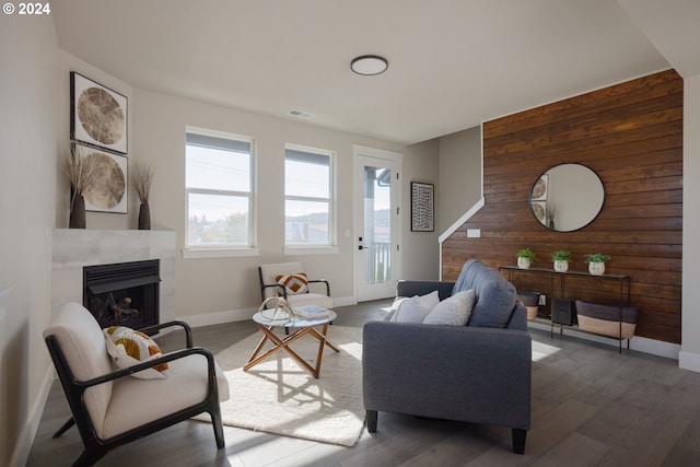 living room with dark wood-type flooring, a tiled fireplace, and wooden walls