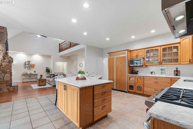 kitchen with ventilation hood, a kitchen bar, a kitchen island, stainless steel microwave, and sink