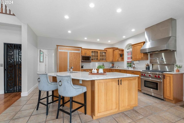 kitchen featuring an island with sink, premium stove, wall chimney range hood, and a breakfast bar area