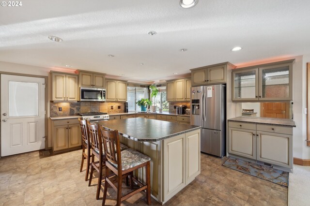 kitchen featuring backsplash, a textured ceiling, a center island, stainless steel appliances, and a breakfast bar area