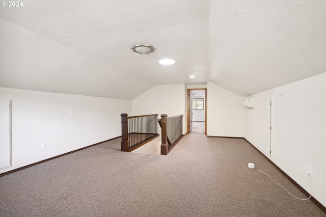 additional living space with lofted ceiling, carpet, a wall mounted air conditioner, and a textured ceiling