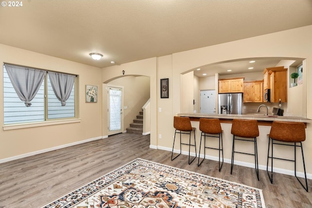 kitchen with hardwood / wood-style flooring, light brown cabinets, a breakfast bar area, and appliances with stainless steel finishes