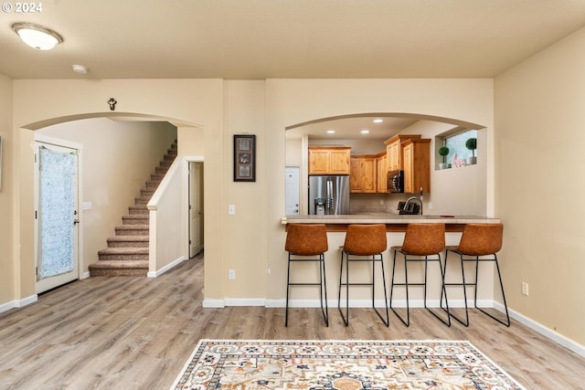 kitchen featuring a breakfast bar, stainless steel fridge, light wood-type flooring, and kitchen peninsula