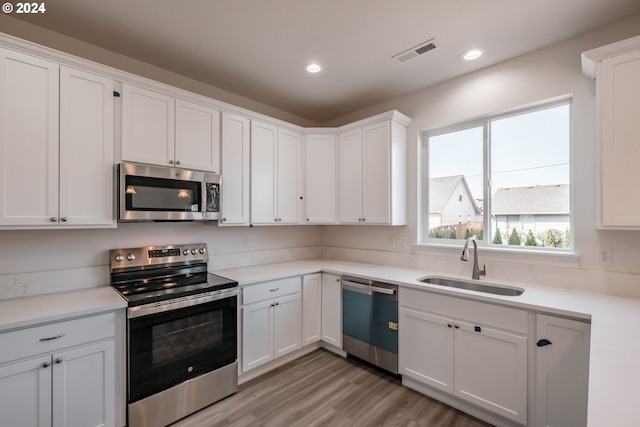 kitchen with appliances with stainless steel finishes, light hardwood / wood-style floors, white cabinetry, and sink