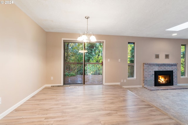 unfurnished living room with a fireplace, light hardwood / wood-style floors, plenty of natural light, and a chandelier