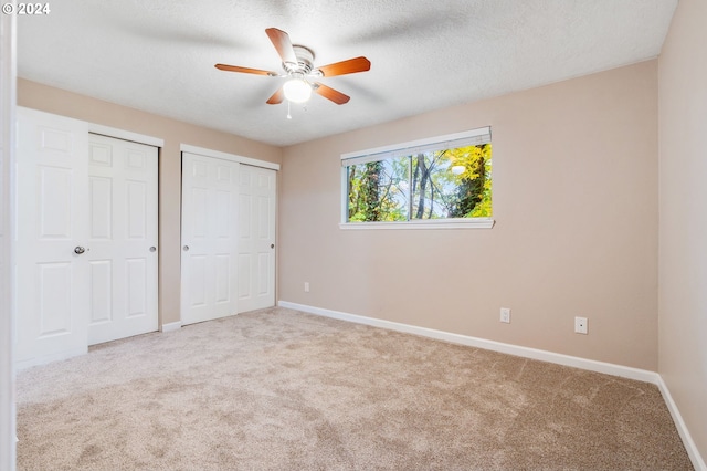 unfurnished bedroom featuring a textured ceiling, ceiling fan, light carpet, and multiple closets